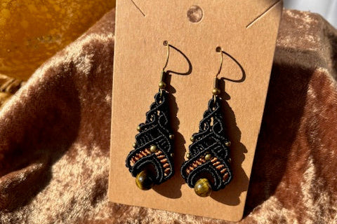Pair of black and gold earrings on a brown card against a textured brown background